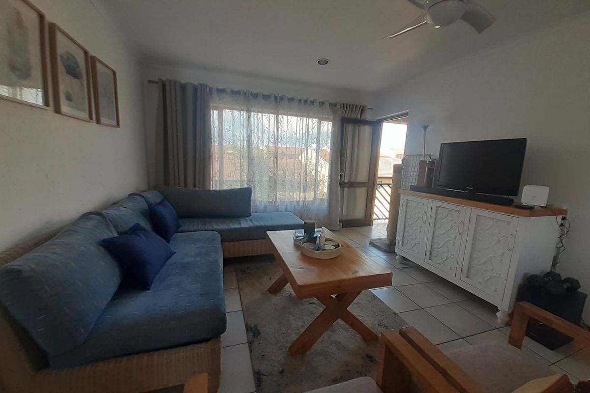 A comfortable living room featuring tiled flooring, a ceiling fan, and direct access to an outdoor balcony area through a sliding door.
