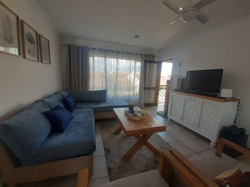 A comfortable living room featuring tiled flooring, a ceiling fan, and direct access to an outdoor balcony area through a sliding door.