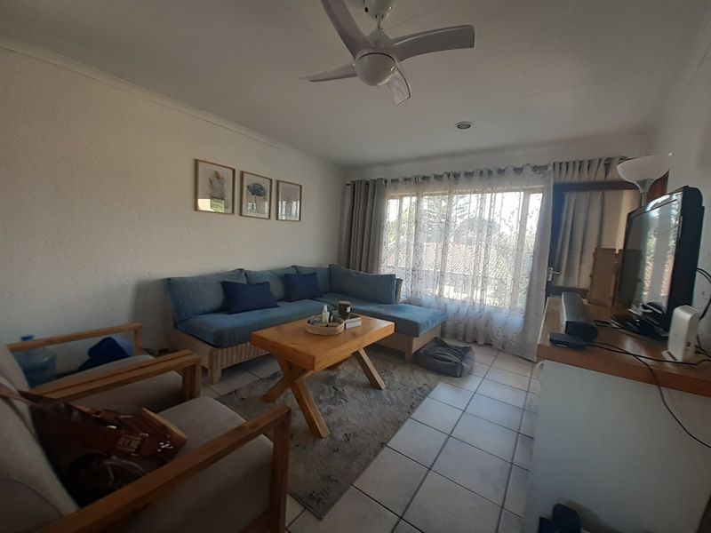 A living room featuring tiled flooring, a ceiling fan, and natural light through large windows.