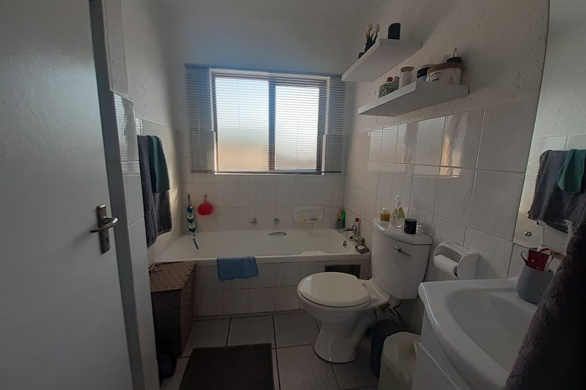 A functional bathroom featuring a built-in bathtub, pedestal basin, and toilet, finished with white wall tiles and tiled flooring.