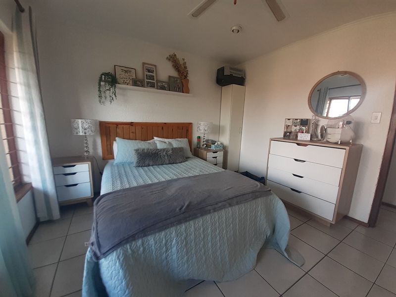 A well-lit bedroom featuring tiled flooring, a ceiling fan, and a built-in cupboard, offering a comfortable and functional living space.