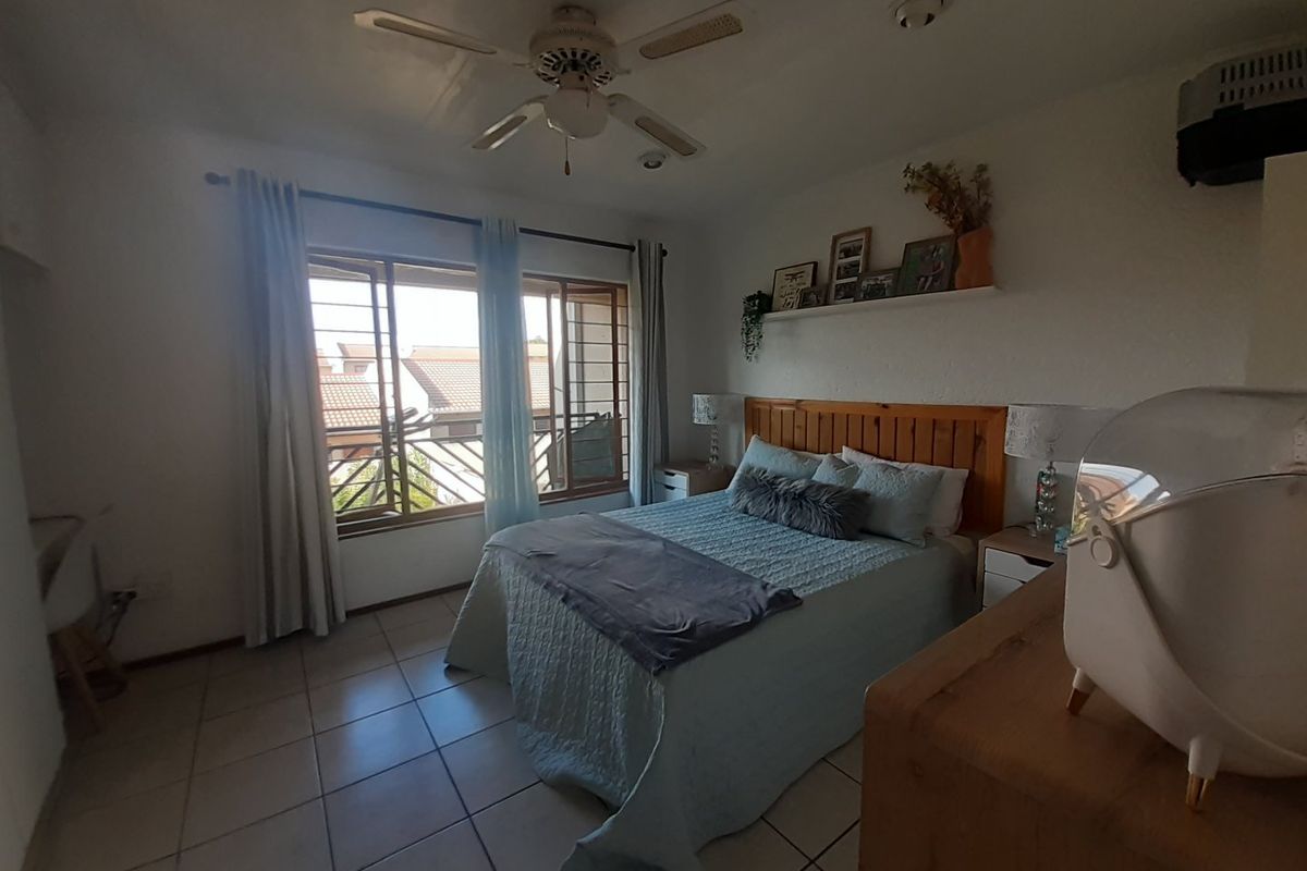 A functional bedroom featuring tiled flooring, a ceiling fan, and large windows with security bars, providing natural light and ventilation.