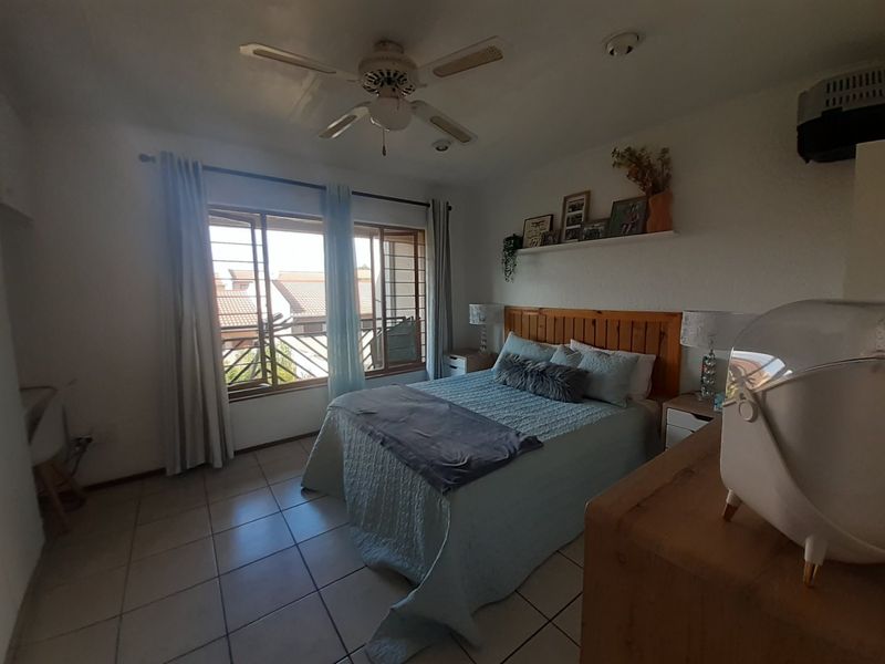 A functional bedroom featuring tiled flooring, a ceiling fan, and large windows with security bars, providing natural light and ventilation.