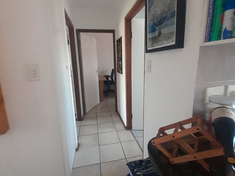 A functional apartment hallway featuring tiled flooring and recessed lighting, providing access to adjacent rooms.