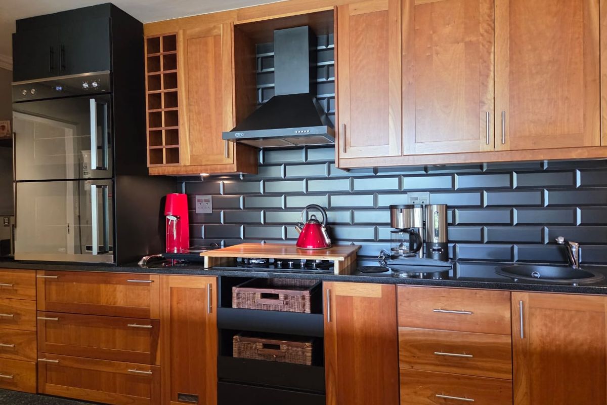 Modern kitchen featuring warm wooden cabinetry, contrasting black subway tile backsplash, granite countertops, and integrated stainless steel oven and extractor fan.
