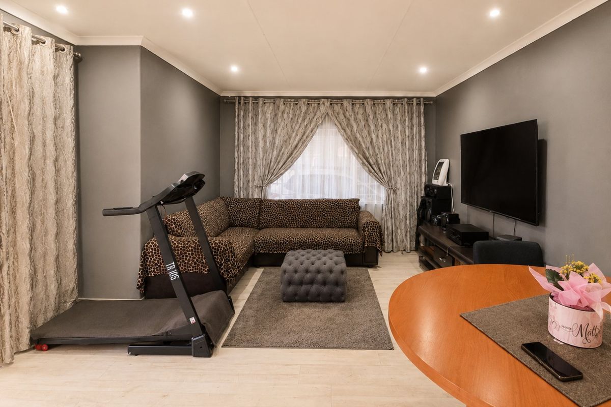 A well-maintained living room featuring neutral grey walls, recessed downlighting, and light-toned laminate flooring, providing a comfortable and functional living space.