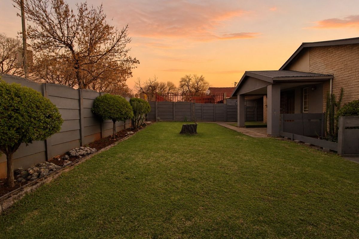 A spacious rear garden featuring a well-maintained lawn, a covered patio area, and secure perimeter walling at sunset.