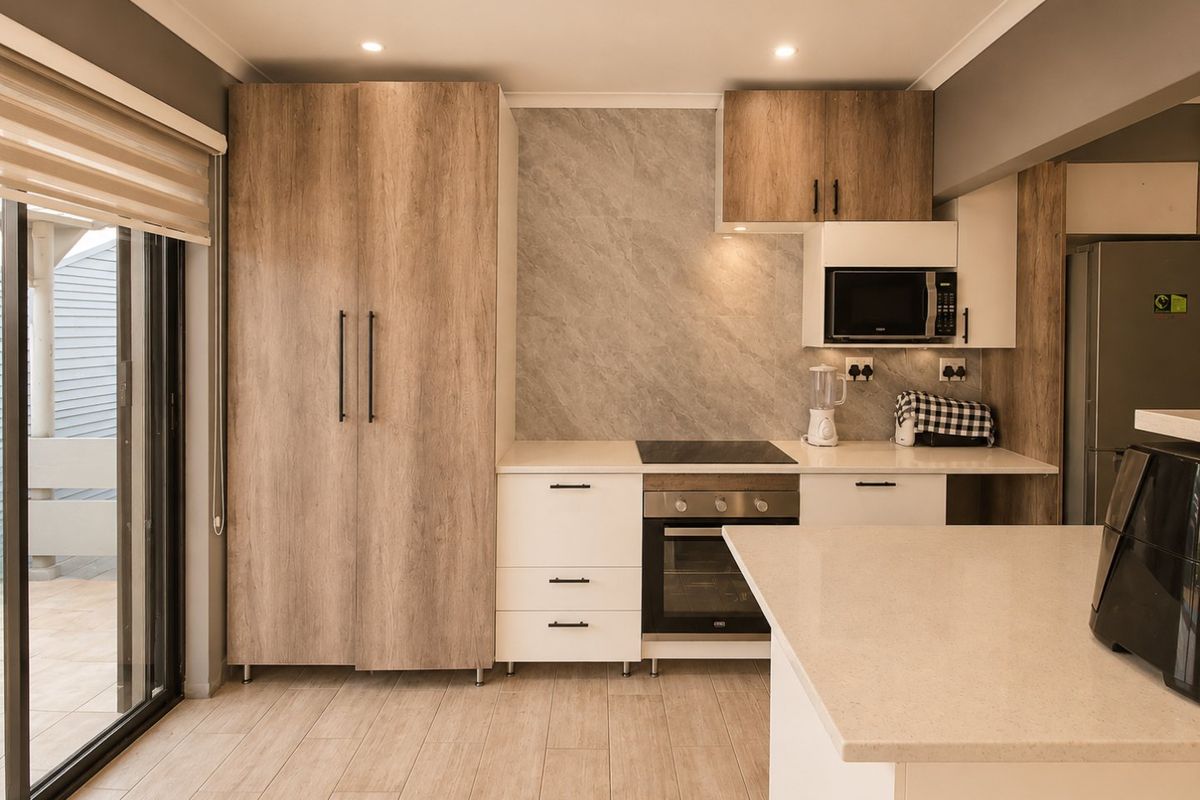Modern kitchen featuring wood-look and white cabinetry, stone benchtops, integrated appliances, and a stone splashback, with direct access to an outdoor patio area.