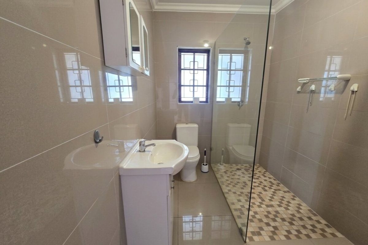 Modern bathroom featuring a walk-in shower with glass screen, pedestal basin, toilet, and neutral floor-to-ceiling tiling.