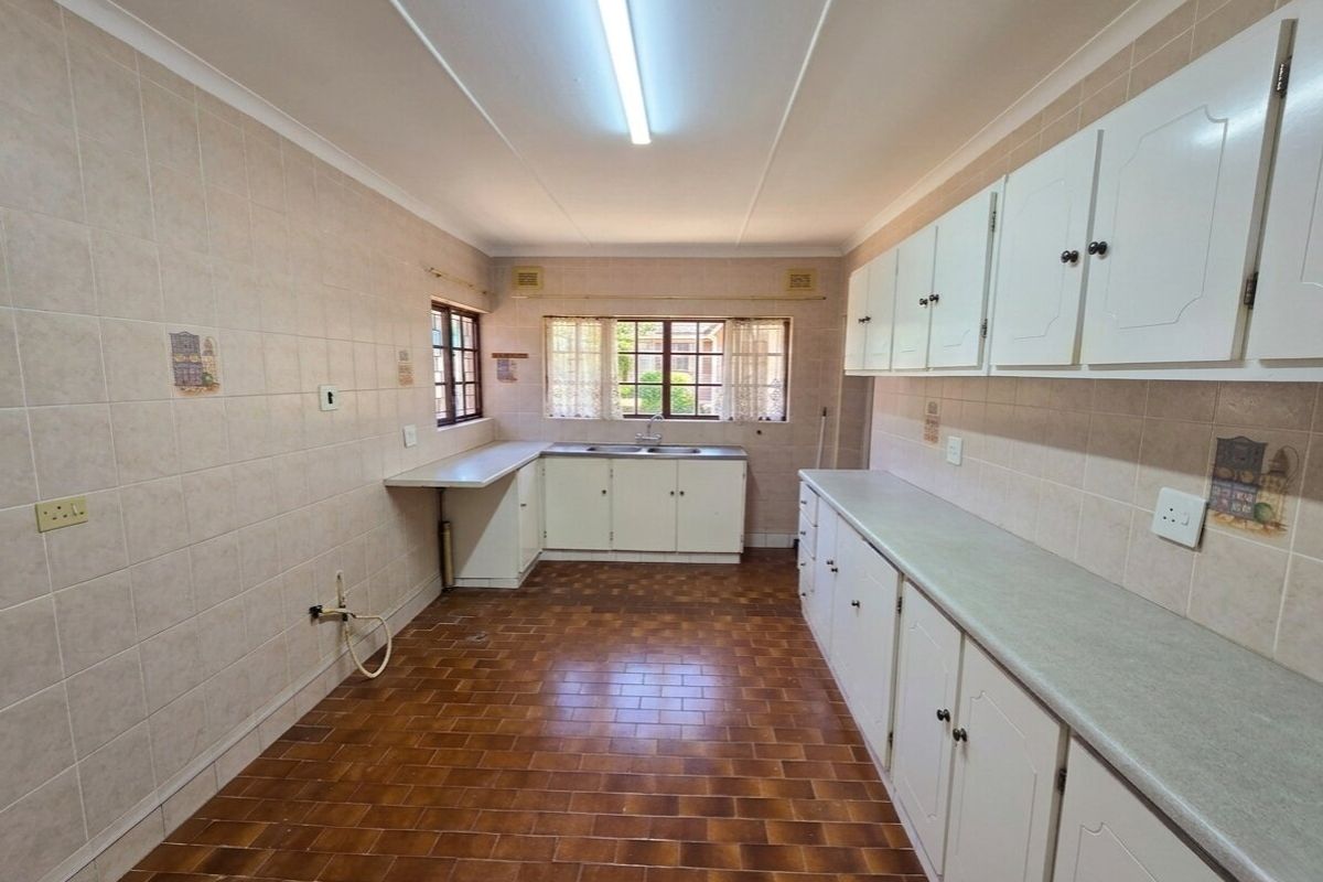 A spacious, empty kitchen featuring extensive built-in cabinetry, laminate countertops, a double sink, and tiled finishes throughout, offering a blank canvas for renovation.
