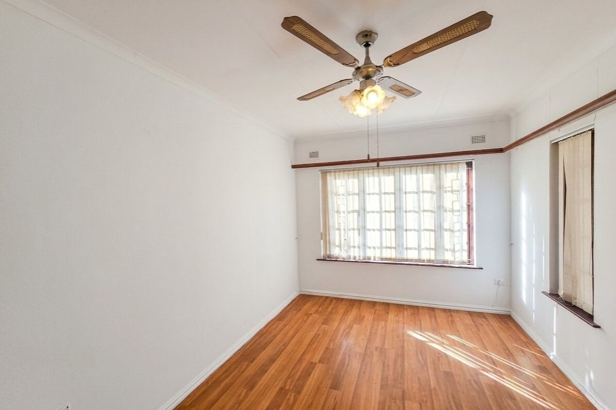 A bright, empty bedroom featuring laminate flooring, a ceiling fan, and window blinds, offering a clean canvas for personalization.