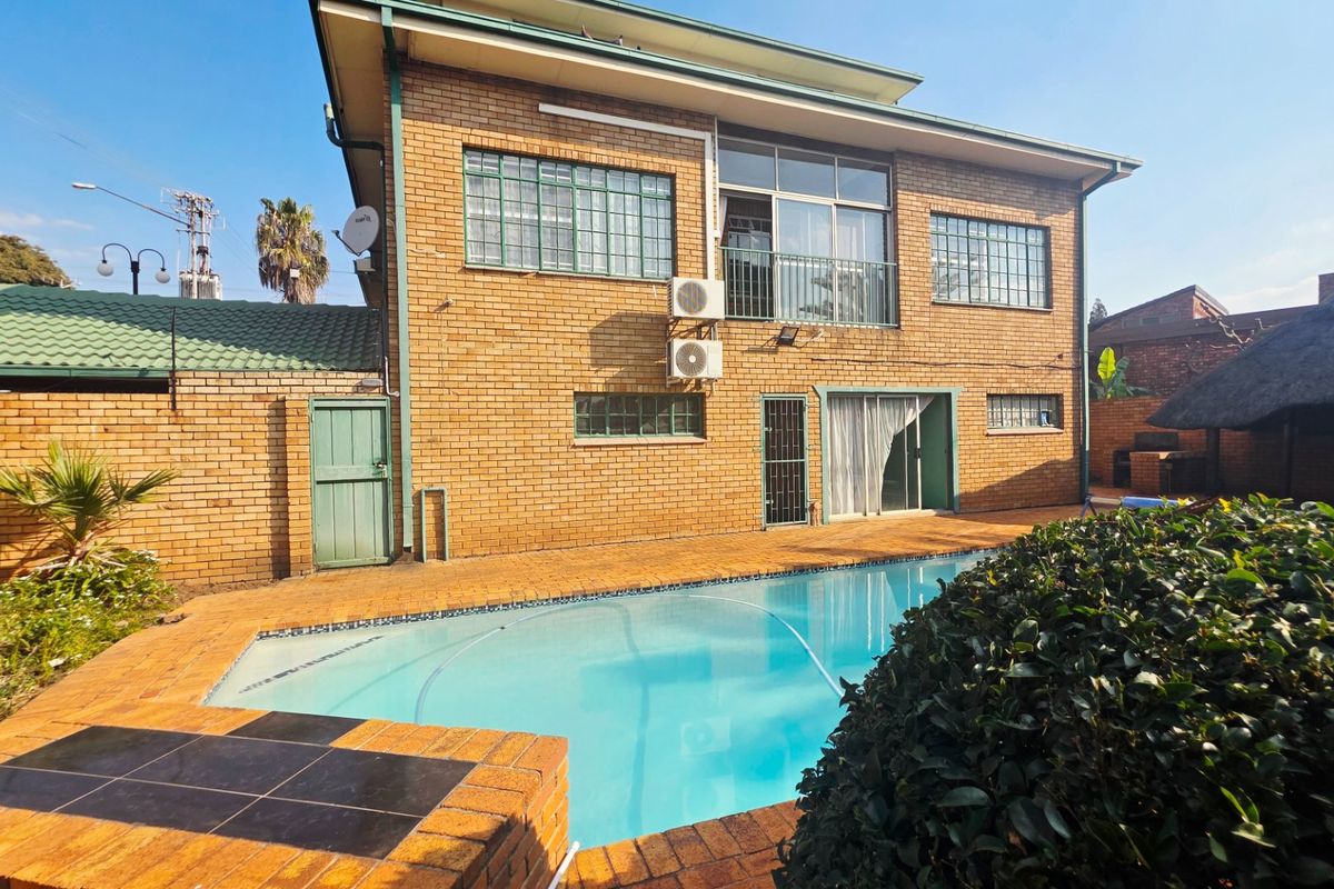 Rear view of a double-story brick house featuring a swimming pool, paved patio area, and balcony access.