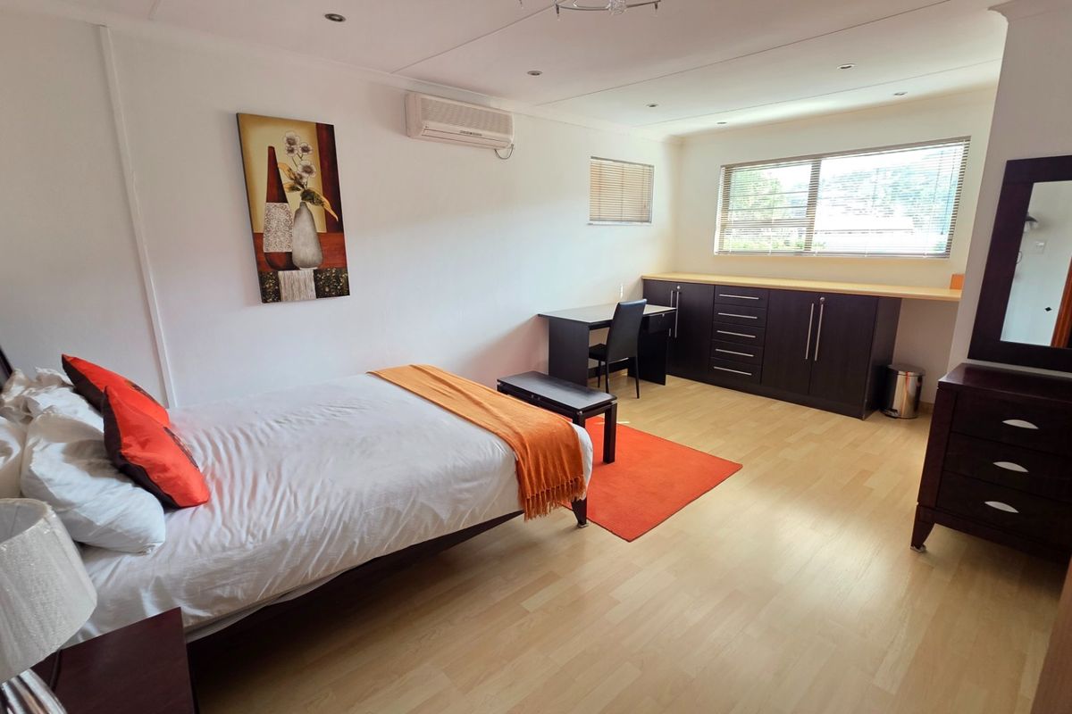 A well-maintained bedroom featuring laminate flooring, recessed downlighting, a split-system air conditioner, and integrated built-in cabinetry for storage.