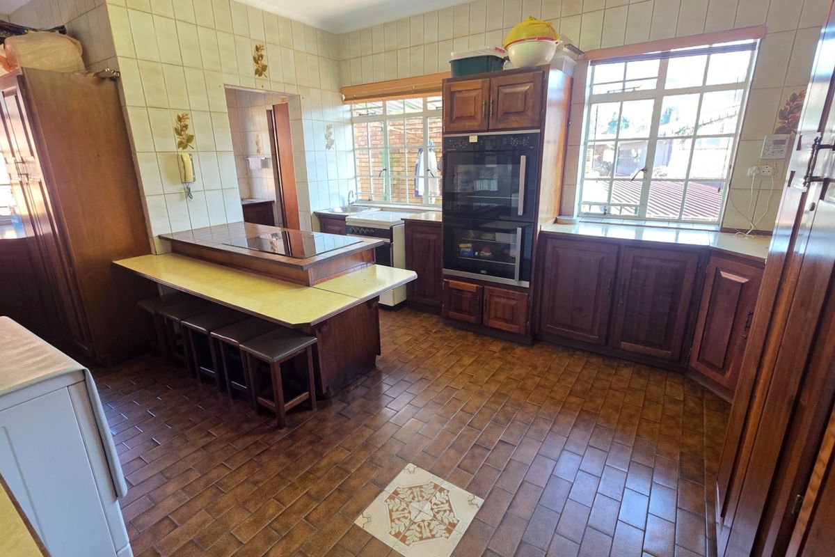 A spacious, traditional kitchen featuring extensive wooden cabinetry, a built-in double oven, ceramic tile flooring, and a functional breakfast bar area.