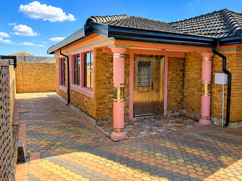 A well-maintained single-story home featuring a face brick exterior, decorative columns, a secure entrance door, and a neatly paved driveway.
