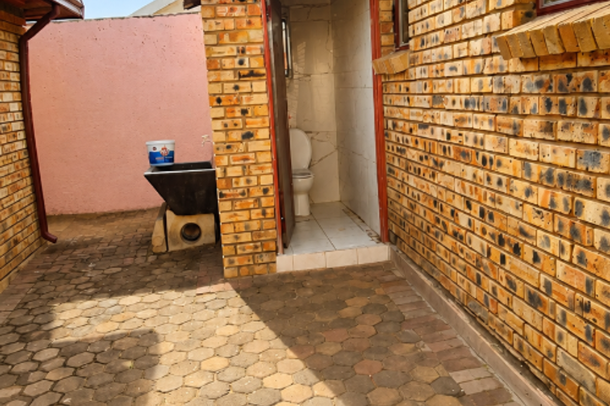 Rear courtyard area featuring face brick walls, paved flooring, and an external toilet facility with an adjacent wash basin.