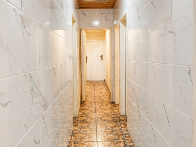A long hallway featuring marble-effect wall tiles, stone-patterned floor tiles, and a warm timber-paneled ceiling with integrated lighting.