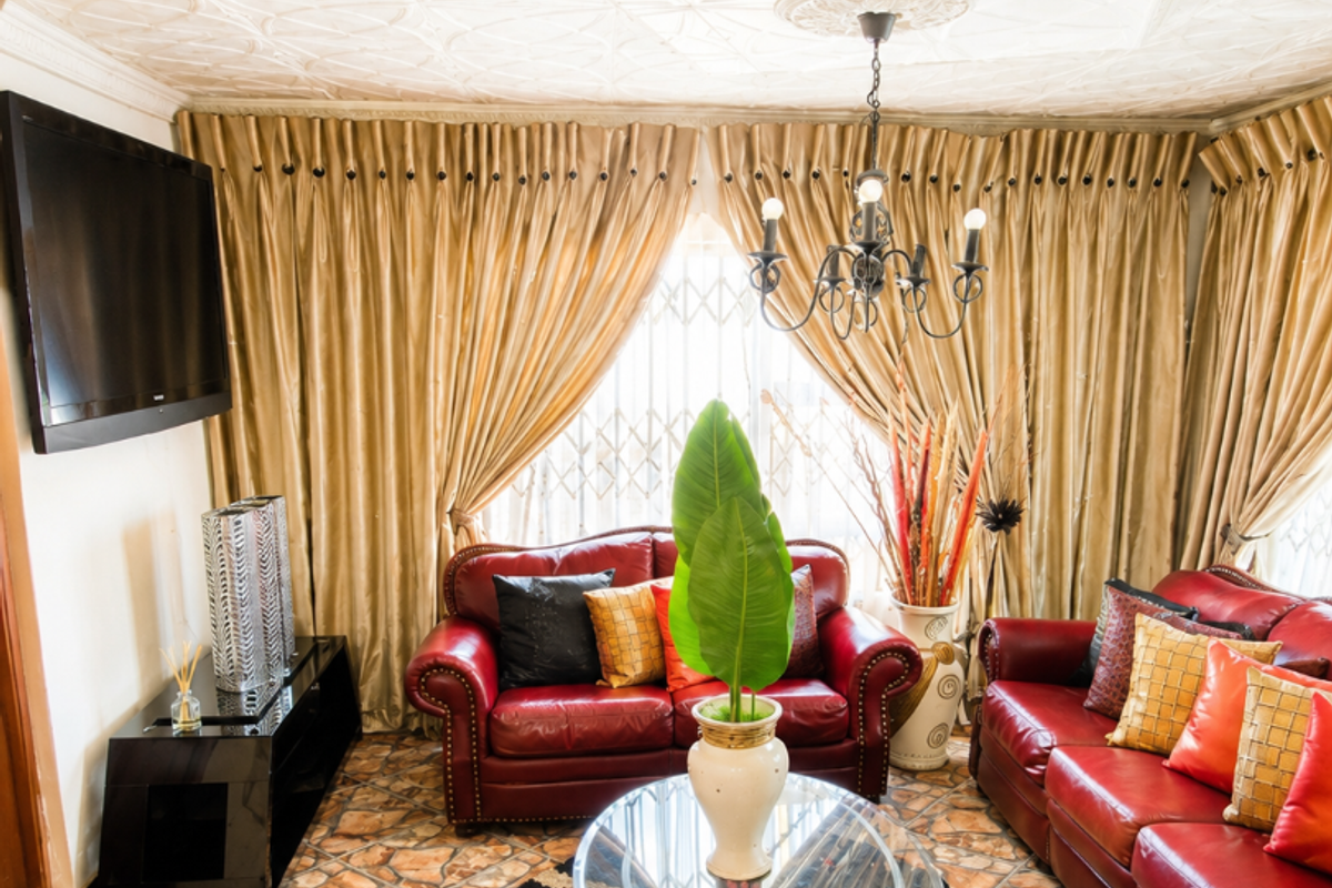 A living room featuring a decorative patterned ceiling, a central chandelier, and tiled flooring, providing a distinct traditional aesthetic.