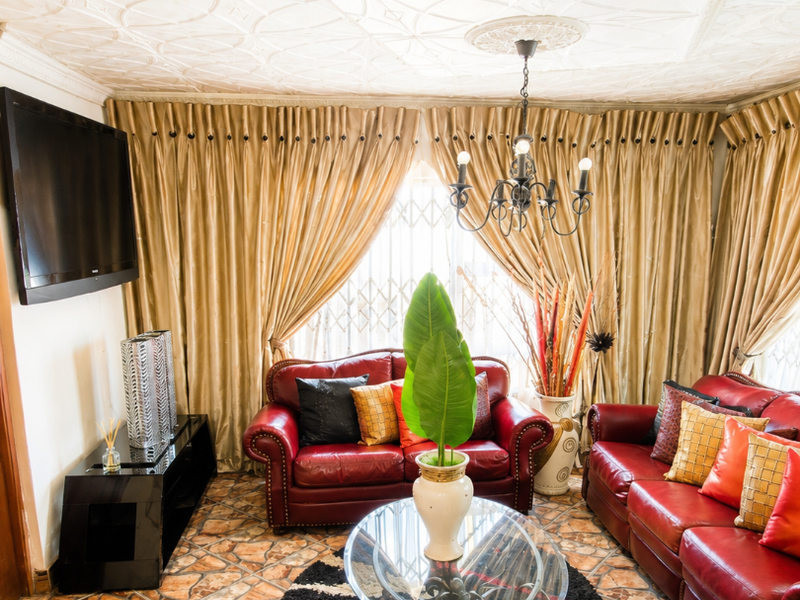 A living room featuring a decorative patterned ceiling, a central chandelier, and tiled flooring, providing a distinct traditional aesthetic.