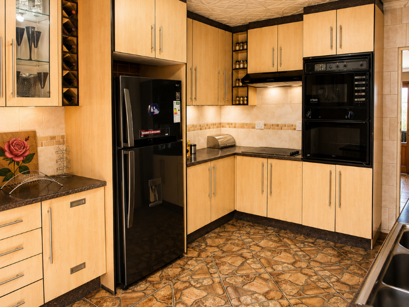 A functional kitchen featuring light wood cabinetry, built-in appliances, decorative ceiling tiles, and distinctive stone-look tiled flooring.