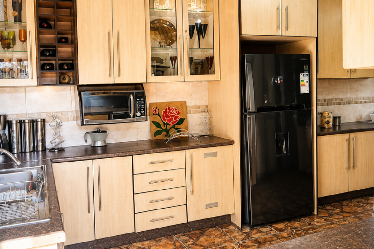 A functional kitchen featuring light wood cabinetry, dark laminate countertops, built-in microwave, and distinctive patterned floor and ceiling tiles.