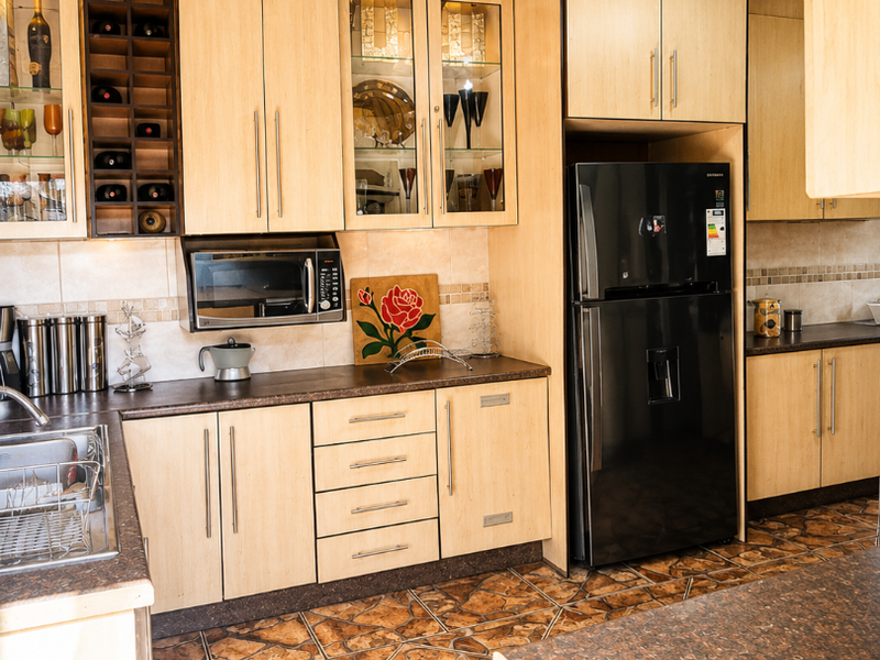 A functional kitchen featuring light wood cabinetry, dark laminate countertops, built-in microwave, and distinctive patterned floor and ceiling tiles.