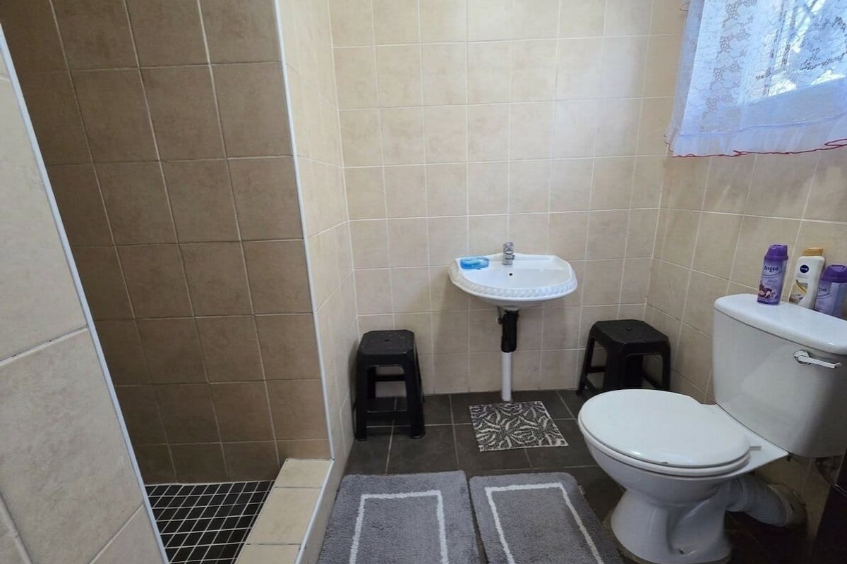 A functional bathroom featuring a shower enclosure, wall-mounted basin, and toilet with neutral ceramic wall and floor tiling.