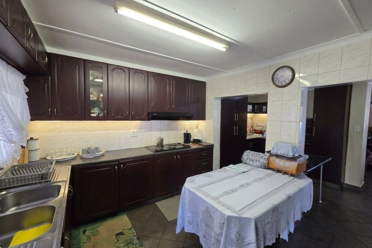 A functional kitchen featuring dark wood cabinetry, laminate countertops, a double stainless steel sink, and a built-in hob with an extractor fan.