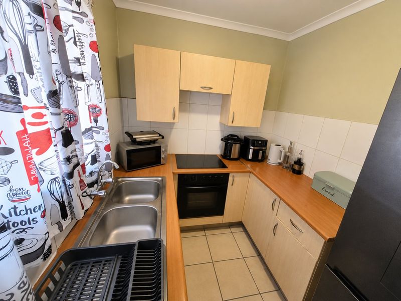 A compact kitchen featuring light wood cabinetry, laminate countertops, a built-in oven with a ceramic hob, and a double stainless steel sink.