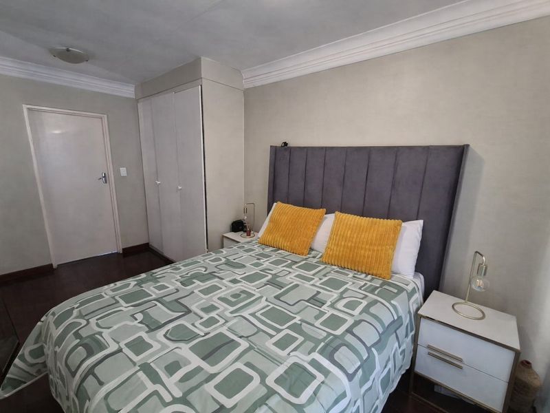 A bedroom featuring built-in cupboards, dark laminate flooring, and decorative ceiling cornicing.
