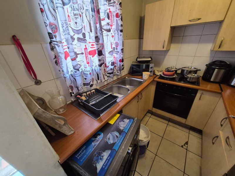 Compact kitchen featuring built-in wooden cabinetry, a double sink, integrated oven, and hob with tiled splashbacks and flooring.