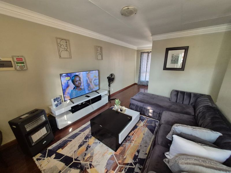 A comfortable living room featuring dark wood-look flooring, crown molding, and a neutral wall finish, providing a functional space for relaxation.