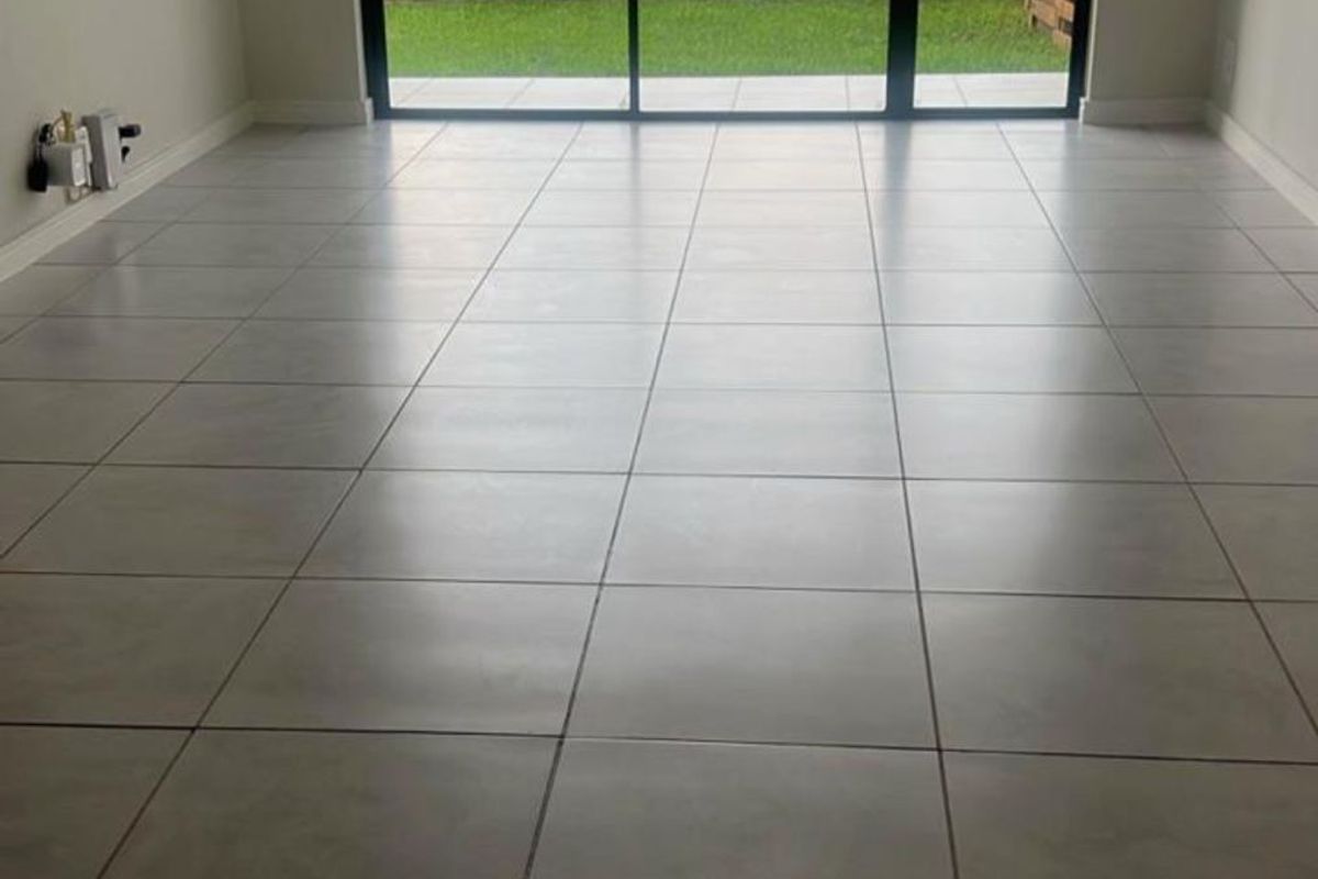 An empty, bright living area featuring large sliding glass doors that open to a private outdoor space with tiled flooring throughout.