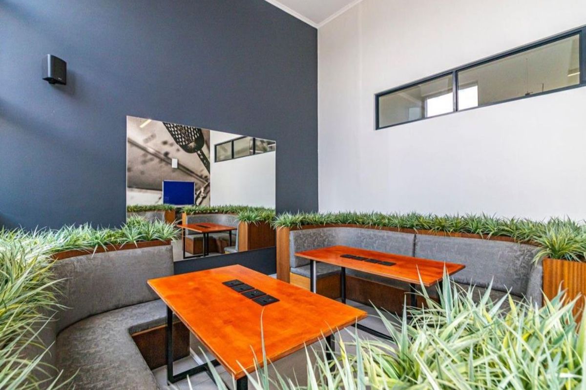 Modern open-plan communal area featuring built-in booth seating with integrated power outlets, high ceilings, and large clerestory windows for natural light.