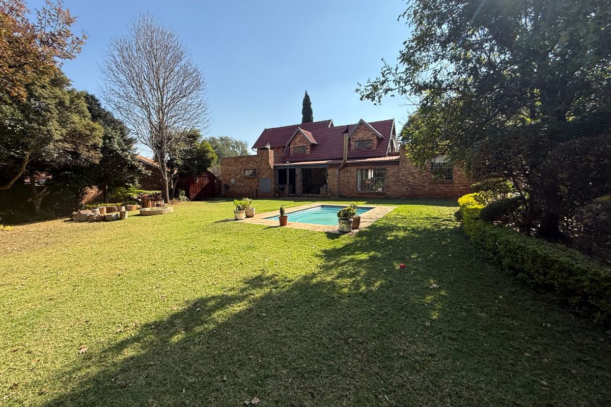 Rear view of a brick house featuring a well-maintained garden and a swimming pool set in a spacious lawn area.