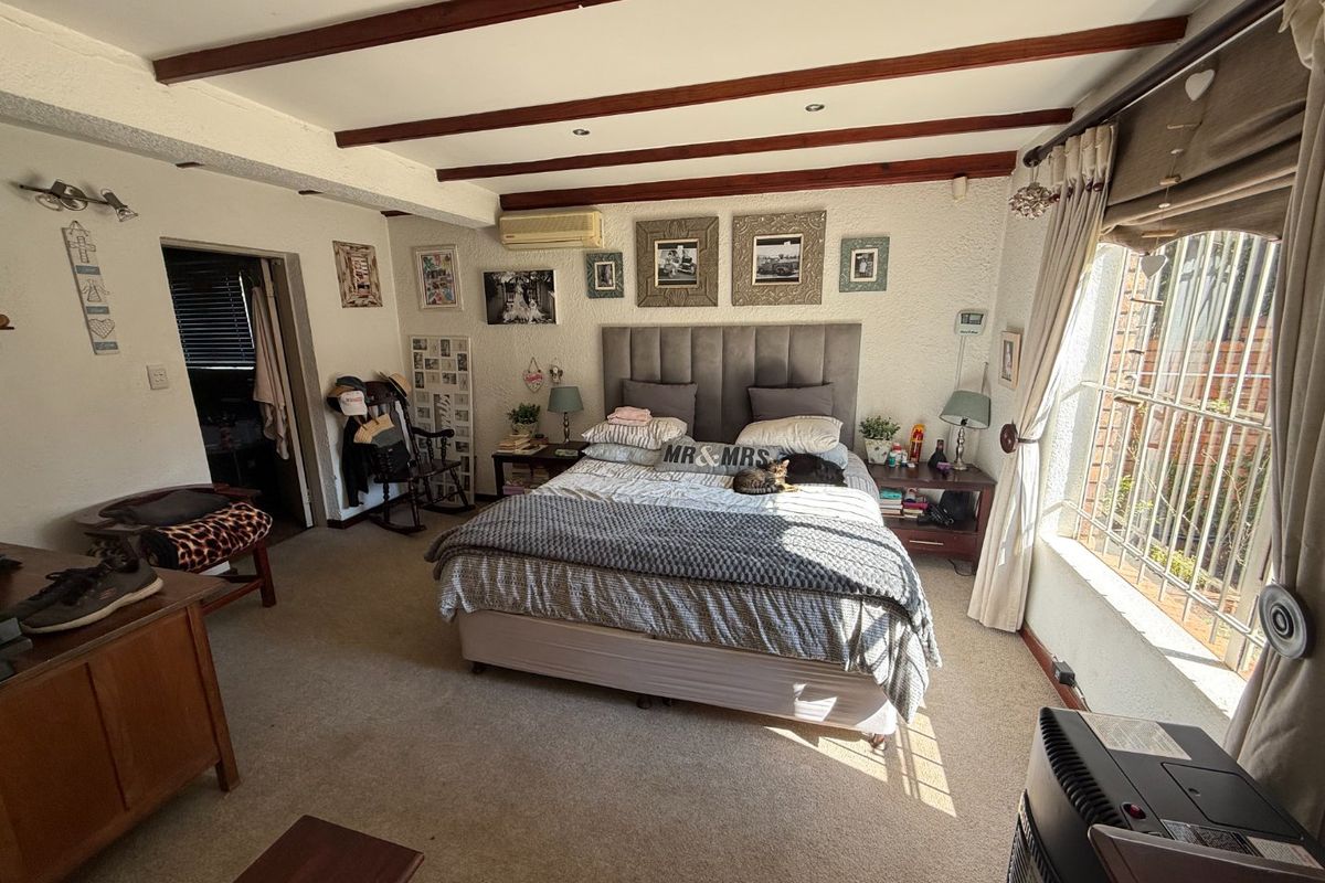 Spacious bedroom featuring exposed timber ceiling beams, wall-mounted air conditioning, and large windows with security bars, offering a functional layout with potential for modernization.
