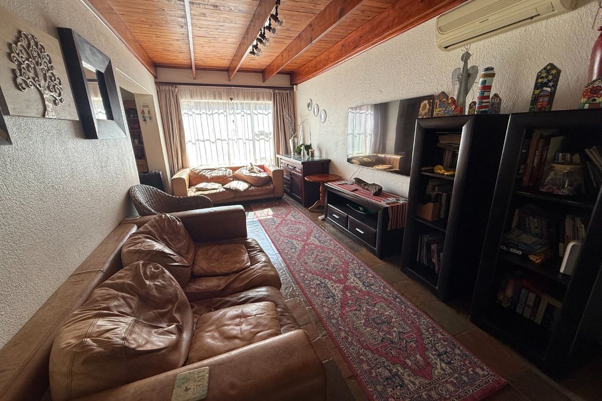 A cozy living room featuring a distinctive exposed timber beam ceiling, tiled flooring, and a wall-mounted air conditioning unit for climate control.