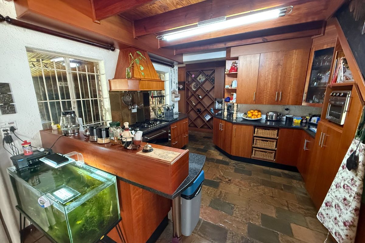 A rustic kitchen featuring extensive wooden cabinetry, stone countertops, exposed timber ceiling beams, and stone tile flooring with a built-in oven and gas cooktop.