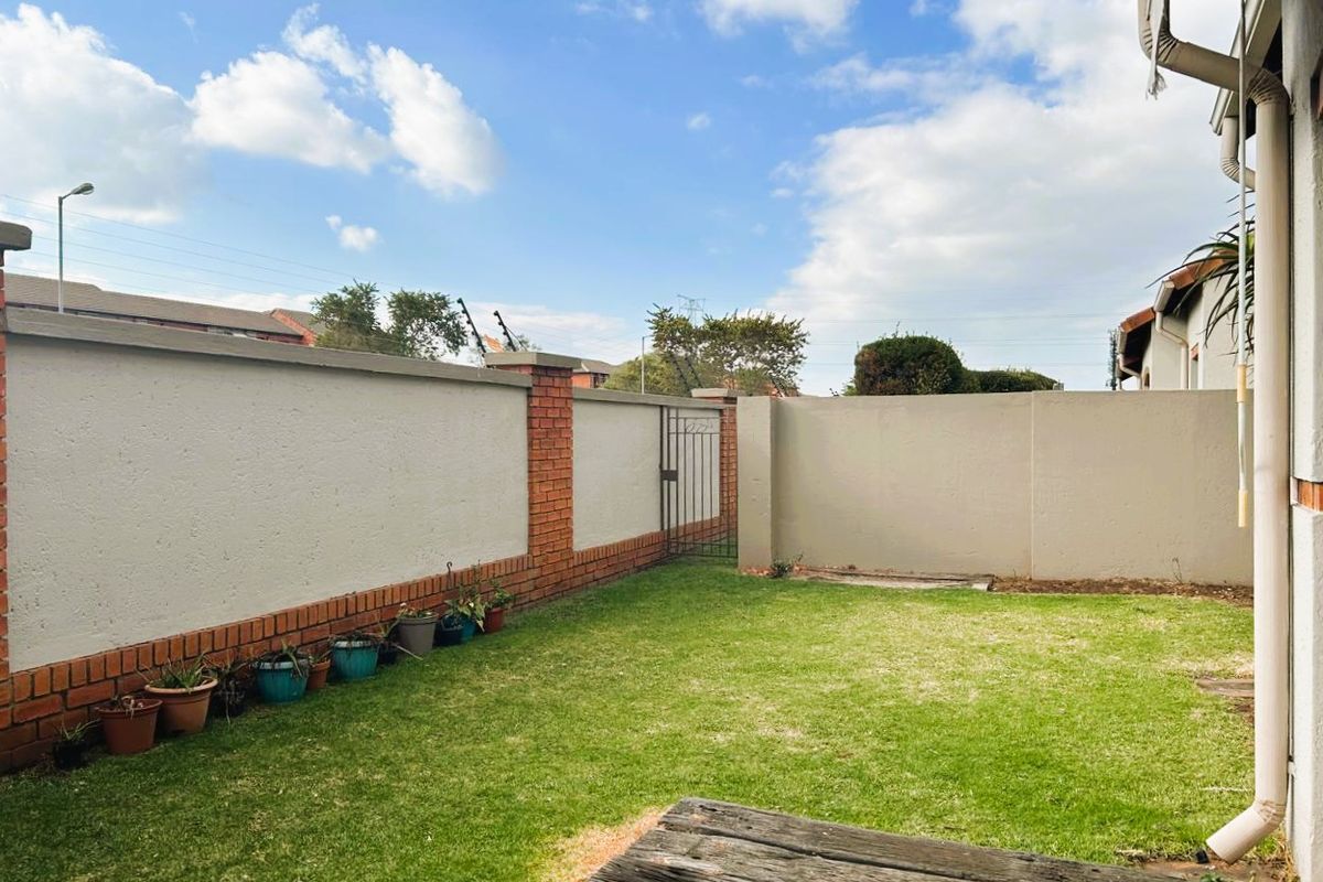 A private rear garden area featuring a well-maintained lawn enclosed by brick and plastered boundary walls with a secure metal pedestrian gate.