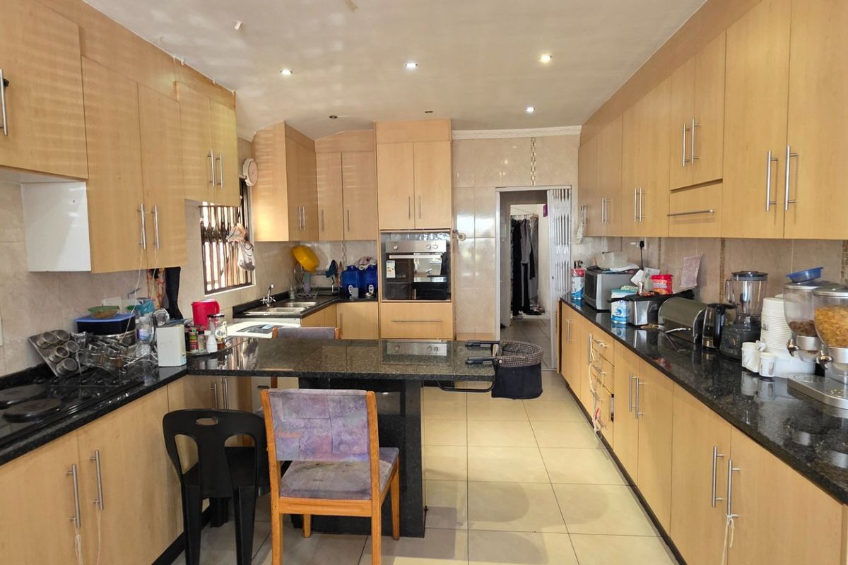 A functional galley-style kitchen featuring light wood cabinetry, dark granite countertops, built-in oven, electric hob, and tiled flooring throughout.