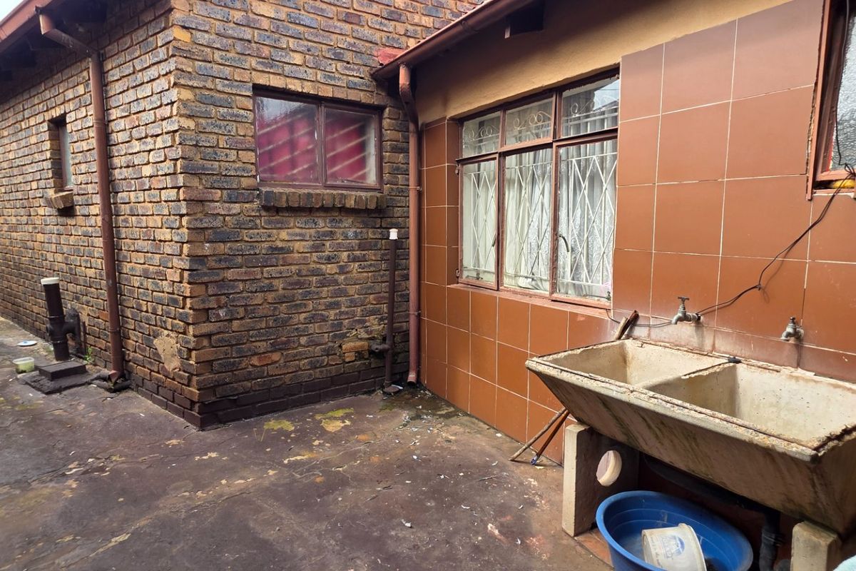 Rear exterior area featuring a concrete laundry trough, brick wall construction, and paved flooring, showing signs of age and weathering.