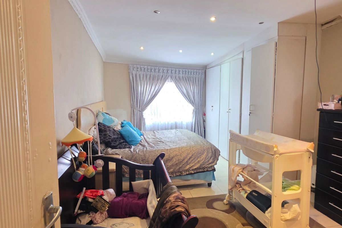 A functional bedroom featuring built-in cupboards, recessed downlighting, and decorative ceiling cornicing, providing a practical layout for a primary or guest sleeping space.