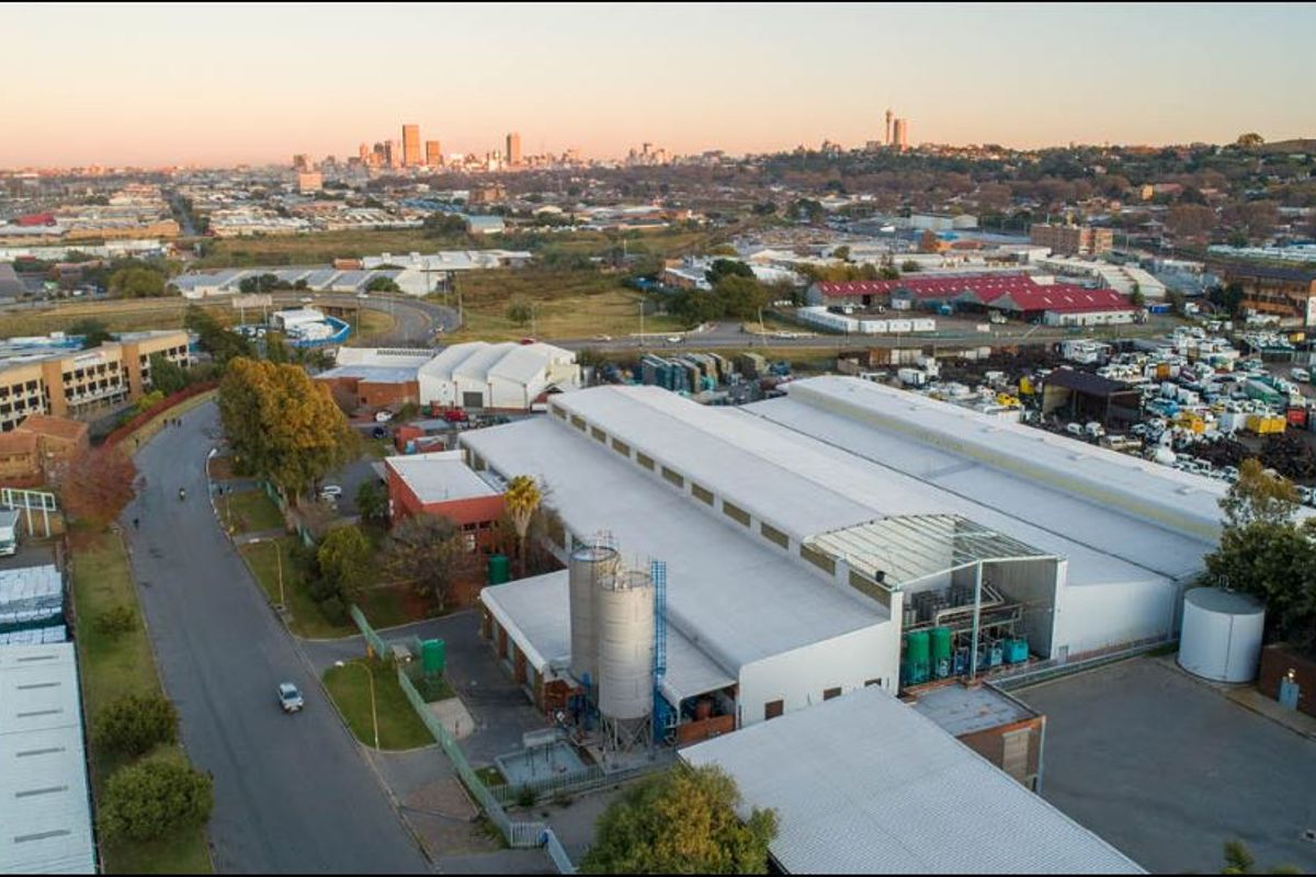 Aerial view of an industrial facility featuring large warehouse structures, storage silos, and a paved yard, situated in an urban industrial zone.