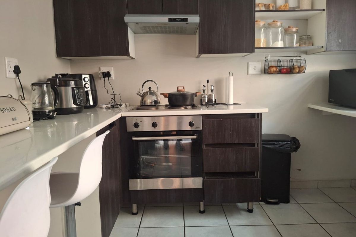 A functional kitchen featuring dark wood cabinetry, stone countertops, built-in oven and hob, extractor fan, and tiled flooring.