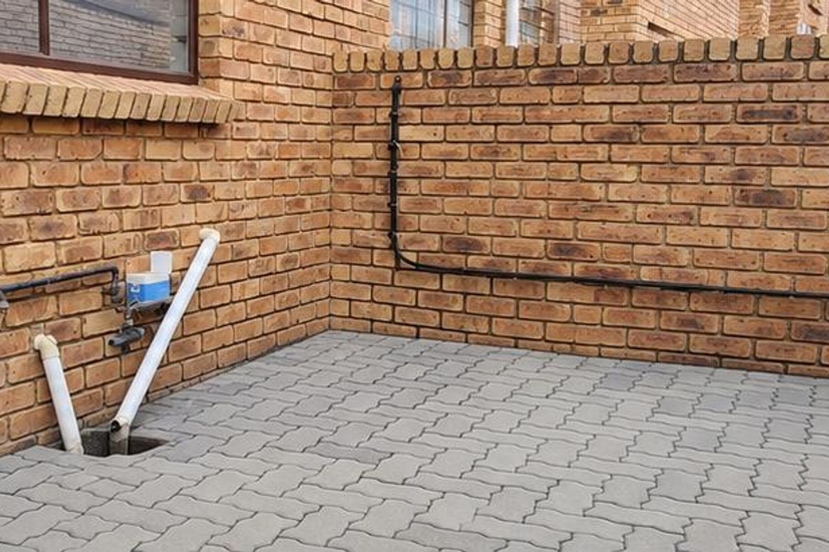 A private rear courtyard area featuring face brick walls, paved flooring, and external utility connections including a wall-mounted washing line.