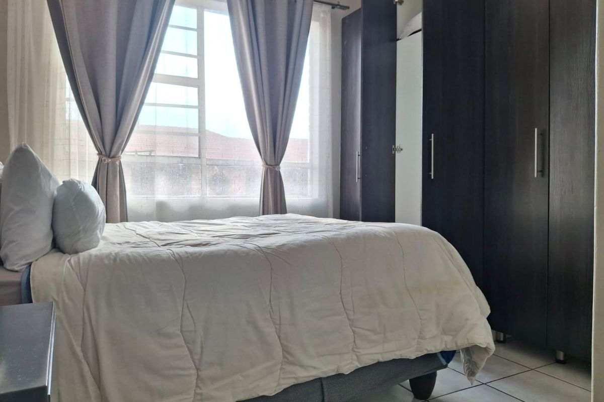 A functional bedroom featuring tiled flooring, a large window for natural light, and dark wood built-in cupboards providing ample storage space.