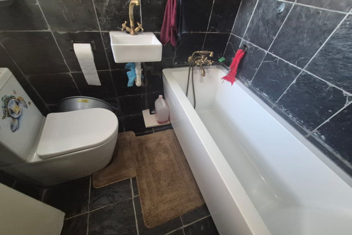 Compact bathroom featuring a bathtub with brass fixtures, a wall-mounted basin, and dark slate tiling throughout.