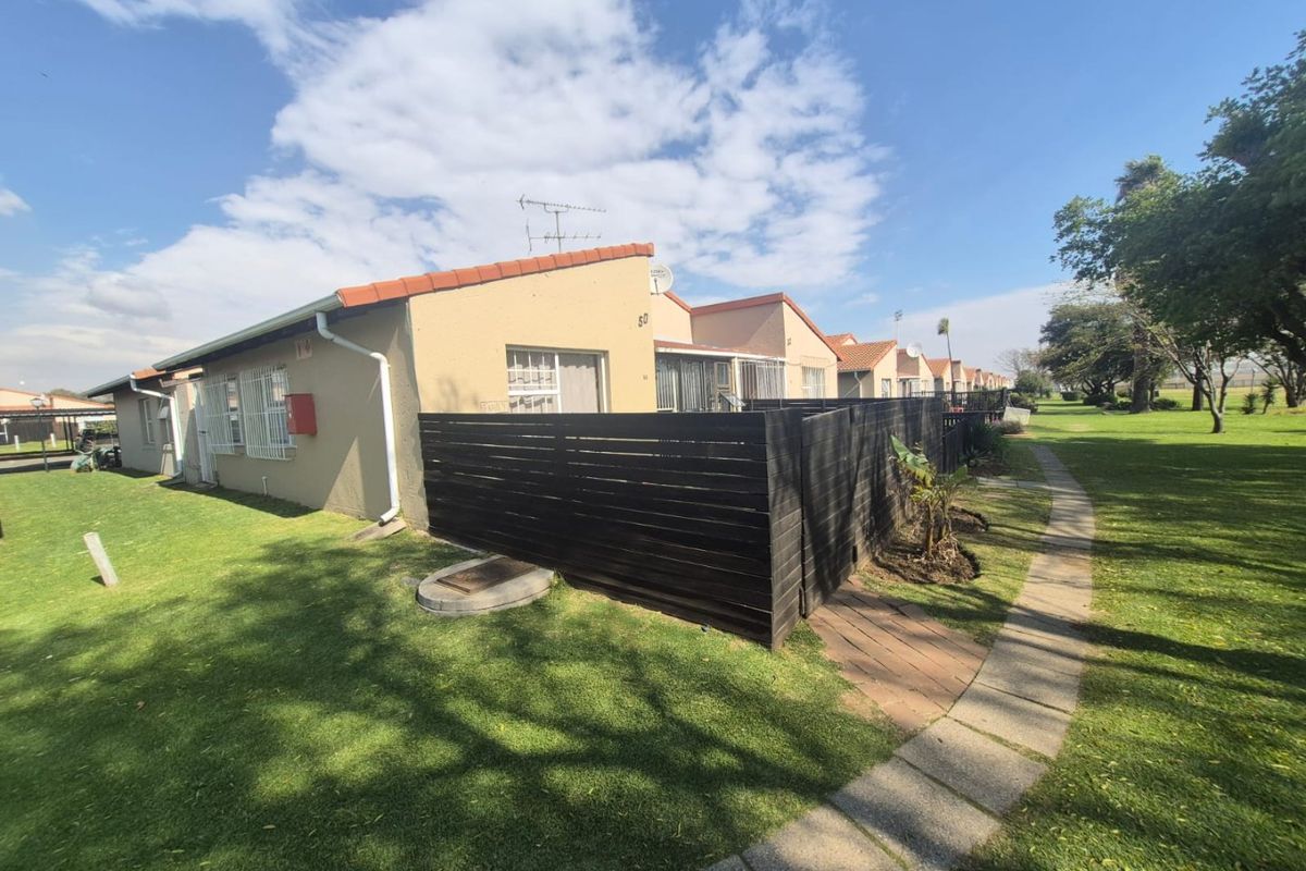 Rear view of a townhouse unit featuring a private fenced patio area, paved walkway, and well-maintained communal garden space.