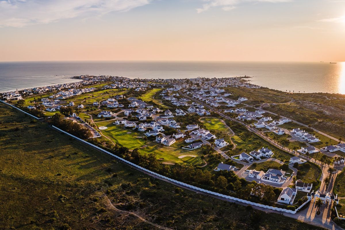 An aerial view of a coastal residential estate featuring a golf course, well-maintained road infrastructure, and proximity to the ocean.