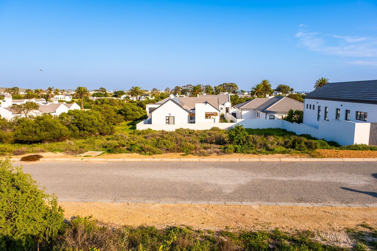A clear street-level view of a residential plot featuring paved road access, kerbing, and surrounding established neighborhood homes.